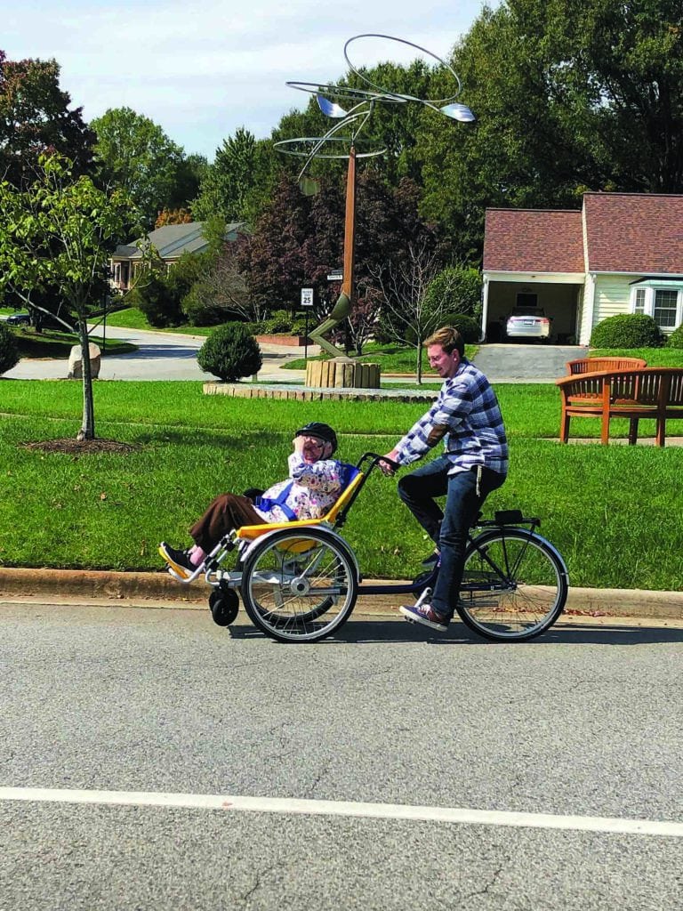 Staff riding wheelchair bike with resident
